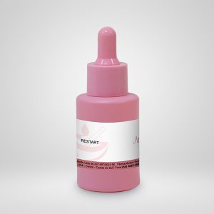 A imagem mostra um frasco conta-gotas de cor rosa, cuja tampa e recipiente têm a mesma coloração. O produto possui uma faixa, no centro, na cor branca e detalhes em um rosa mais escuro. O frasco está posicionado contra um fundo claro.